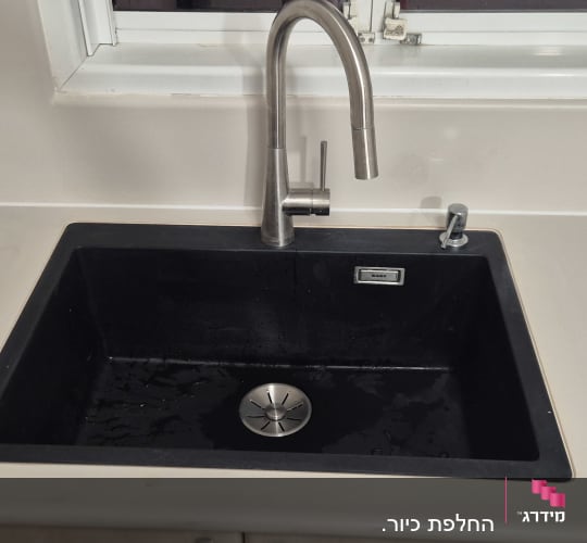כיור מטבח שחור מותקן במשטח שיש בהיר עם ברז נירוסטה